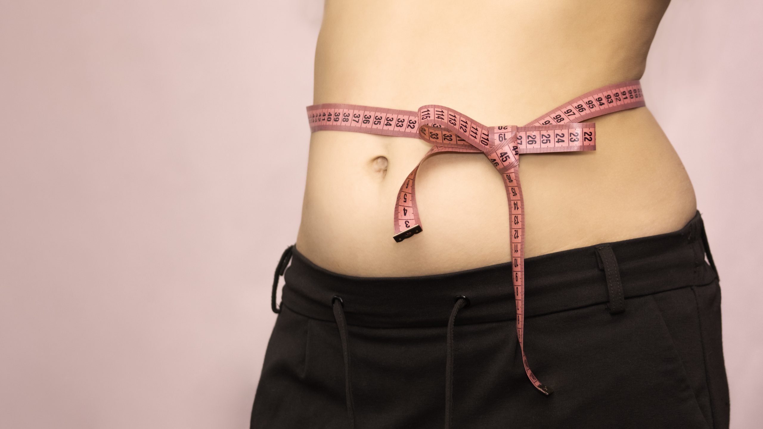 bow of centimeter ribbon on the waist of a woman, the concept of weight loss, healthy lifestyle. layout with copy space.